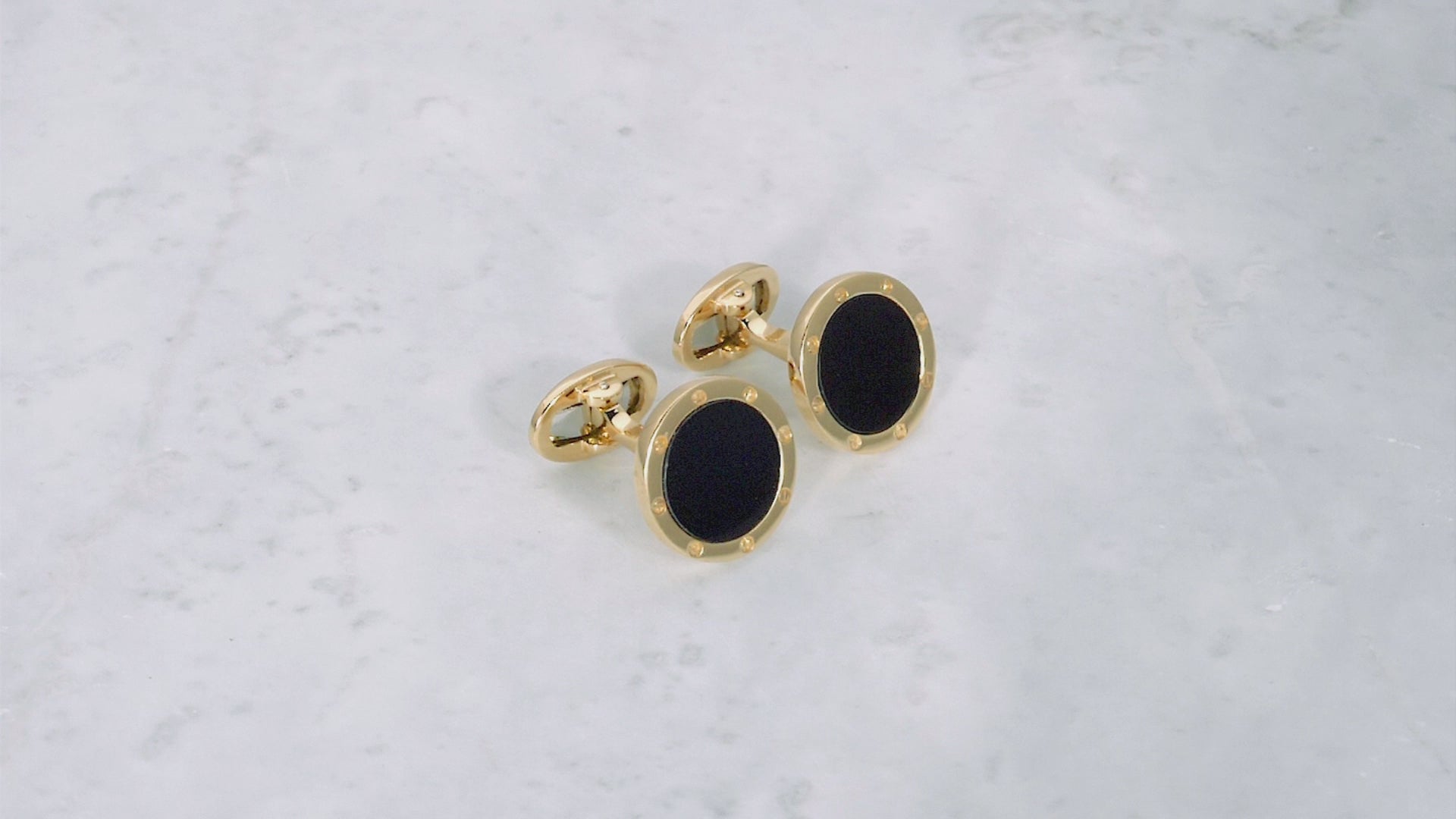 180 degree video of Onyx Gemstone with Rivet Etch Detail 18K Yellow Gold Cufflinks on a marble background.