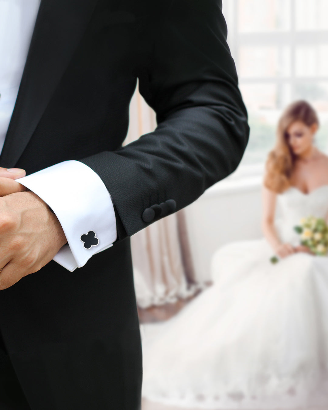 Photo of male models arm and torso in the foreground wearing Jan Leslie's Onyx Gemstone Four Leaf Clover Sterling Silver Cufflinks and Tuxedo Studs on a white tuxedo shirt and black tuxedo jacket with a bride in the background looking down holding a yellow bouquet of roses.