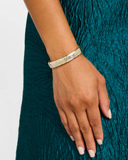 Woman in teal dress wearing 18K gold vermeil white mother-of-pearl petal Seed of Life hinged cuff bangle at wrist showing luminous white MOP exterior face with continuous Seed of Life gold vermeil lattice by Jan Leslie