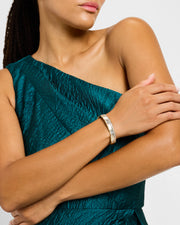 Woman in teal jacquard dress wearing 18K gold vermeil white mother-of-pearl petal Seed of Life hinged cuff bangle at wrist showing luminous white MOP exterior with gold Seed of Life lattice by Jan Leslie