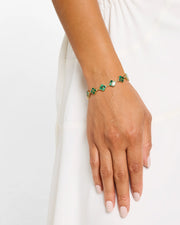 Close-up of woman's wrist wearing gold vermeil sterling silver multi-station malachite floral lattice quatrefoil bracelet with banded green stone inlay petal stations over white draped fabric, Jan Leslie
