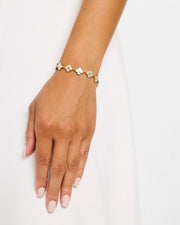 Close-up of woman's wrist wearing gold vermeil sterling silver multi-station white mother of pearl floral lattice quatrefoil bracelet over white draped fabric, Jan Leslie 