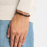 Man in cream sweater and jeans wearing dark brown braided leather bracelet with rose gold clasp — Jan Leslie