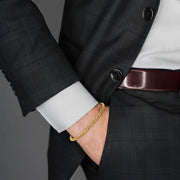 Man in black suit wearing twisted rope gold bracelet with hand in pocket.