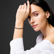 Woman in white off-shoulder top wearing a dark brown braided leather bracelet with gold magnetic clasp.