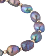 Close-up of iridescent gray and blue baroque freshwater pearls with gold spacer beads showing natural luster and texture.