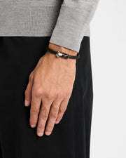 Man in gray sweater wearing a black braided leather bypass bracelet with silver golf bag clasp on his wrist
