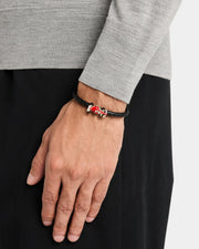 Man wearing sterling silver red enamel Formula 1 racing car clasp double-wrap black braided leather bracelet on wrist with grey knit sleeve by Jan Leslie