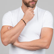 A slim copper-toned twisted cable bracelet with a gunmetal tube bar station worn casually.