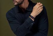 Man in navy shirt stacking navy and brown wide braided leather bracelets with silver clasp — Jan Leslie