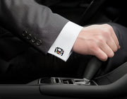  Man wearing sterling silver Formula 1 steering wheel enamel cufflink on white French cuff with grey suit jacket in luxury car interior by Jan Leslie