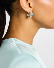 Woman wearing sterling silver blue enamel petal Seed of Life cutwork wide huggie hoop earring close-up showing powder blue enamel ground raised silver Seed of Life cutwork lattice and post-and-butterfly back by Jan Leslie