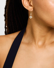 Woman in navy dress wearing 18K gold vermeil white mother-of-pearl petal Seed of Life drop earrings showing luminous white MOP quatrefoil clover pendant with Seed of Life gold lattice and small round white MOP accent stone by Jan Leslie