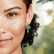 "Woman with curly hair touching her ear wearing a gold huggie hoop earring with quatrefoil turquoise inlay and gold petal overlay
