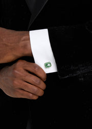 Man in black velvet tuxedo wearing faceted emerald cushion-cut cufflink with silver bezel on white French cuff.