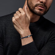 Man in gray sweater wearing a black braided leather bypass bracelet with silver golf bag clasp on his wrist"