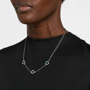 Woman in black crew neck top wearing a sterling silver three-station necklace with open circle blue and teal enamel mosaic pendants.