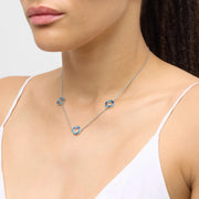 Woman in white camisole wearing a sterling silver three-station necklace with open circle blue and teal enamel mosaic pendants.
