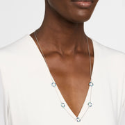 Woman in white v-neck top wearing a long sterling silver station necklace with five open circle blue and teal enamel mosaic pendants.