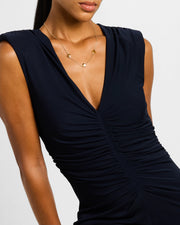  Woman in black deep V-neck dress wearing 18K gold vermeil tiger eye petal Seed of Life three-station necklace at collarbone showing three evenly spaced warm amber-brown chatoyant tiger eye quatrefoil clover stations with Seed of Life gold cutwork lattice on fine gold cable chain by Jan Leslie
