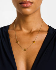 Woman in black dress wearing 18K gold vermeil tiger eye petal Seed of Life three-station necklace showing three warm amber-brown tiger eye quatrefoil clover stations at collarbone by Jan Leslie