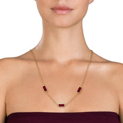 Woman in burgundy strapless dress wearing a gold cable chain station necklace with three rectangular carnelian stone pendants in gold bezel settings.