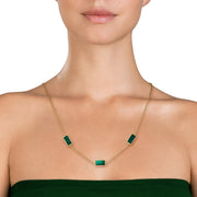 Woman in emerald green strapless dress wearing a gold cable chain station necklace with three rectangular malachite stone pendants in gold bezel settings.