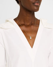 Woman wearing 18K gold vermeil white mother-of-pearl petal Seed of Life barrel pendant necklace at collarbone with white V-neck blouse showing luminous white iridescent MOP ground by Jan Leslie