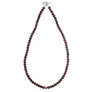 Overhead flat lay of matte red tiger's eye round bead necklace with burgundy and black banded stones, oxidized sterling silver filigree accent bead, and sterling silver toggle clasp, Jan Leslie luxury men's gemstone bead necklace"
