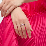 Woman wearing sterling silver segmented pink enamel eternity band ring on middle finger against hot pink pleated satin skirt, Jan Leslie luxury women's fine jewelry lifestyle.