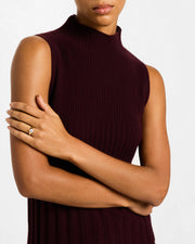 Woman in burgundy ribbed sleeveless mock-neck top with arms crossed wearing gold vermeil sterling silver slim band white mother of pearl floral lattice quatrefoil ring on index finger, Jan Leslie