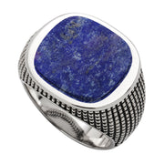 Deep royal blue lapis with characteristic gold pyrite flecks and natural matrix veining — a large, bold cushion cabochon in a polished silver bezel with oxidized arrow-border engraving around the inner edge
