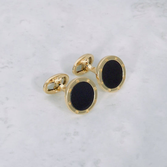 180 degree video of Onyx Gemstone with Rivet Etch Detail 18K Yellow Gold Cufflinks on a marble background. 