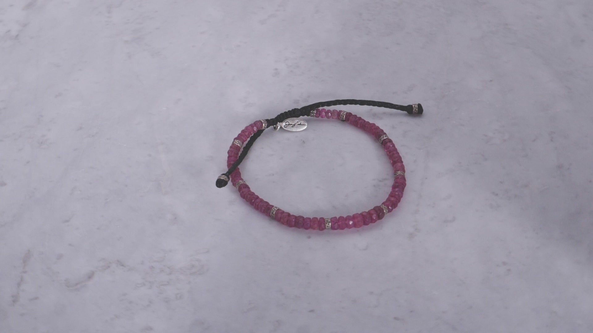 360 video of the an Leslie Faceted Ruby Gemstone Bracelet with Black Pull Cord on marble background. 