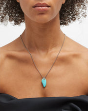 Freeform polished turquoise horn pendant necklace on fine gold curb chain worn at sternum by model 