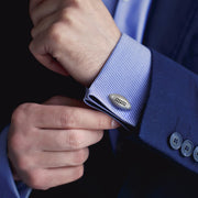 Close up of male models wrist donning Jan Leslie's Football Brushed Sterling Silver Cufflinks on a blue and white striped cuffed shirt and blue suit jacket. 